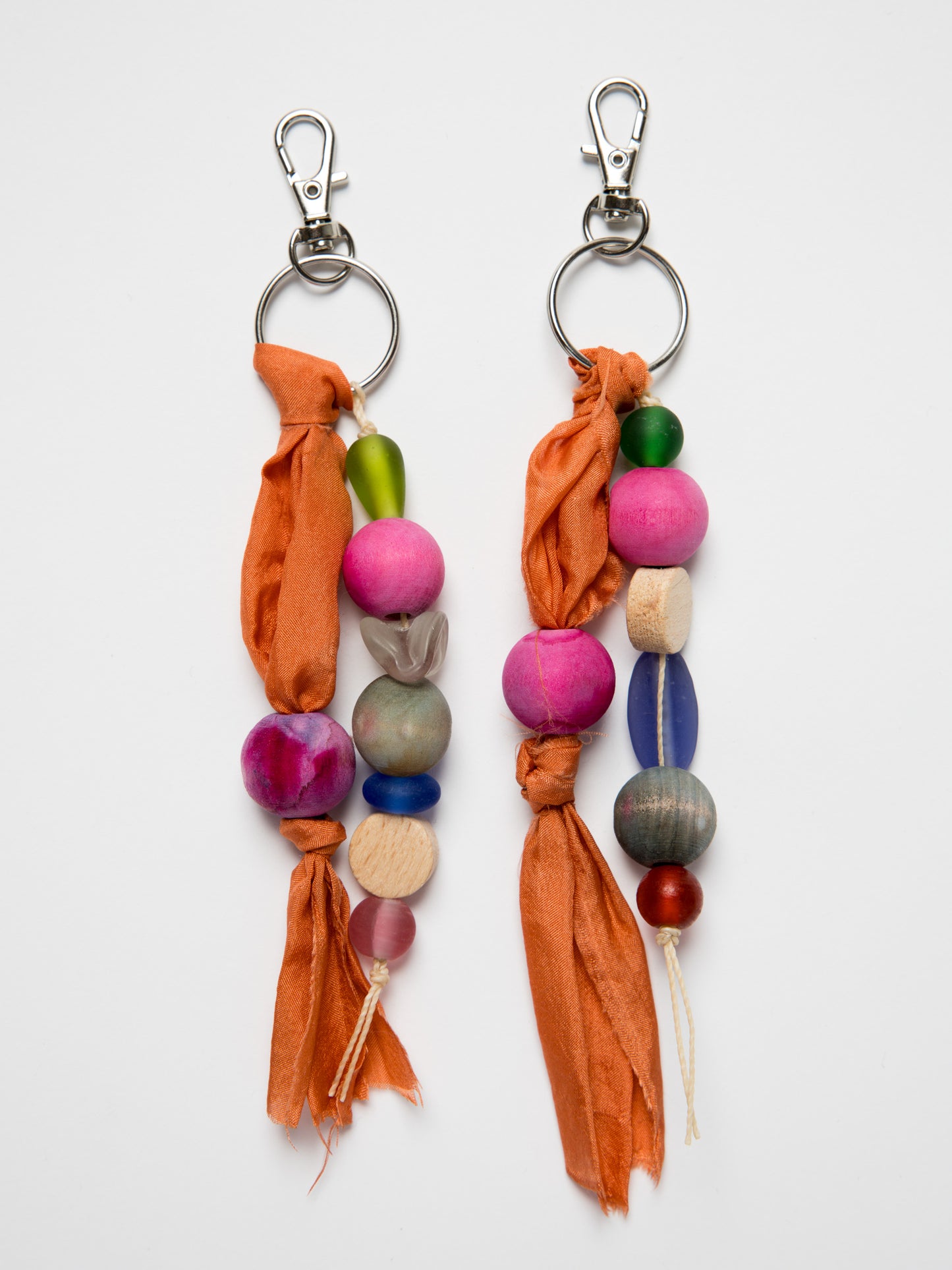 Colorful handmade keychains with wood and glass beads and silk on a white background