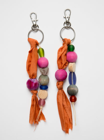 Colorful handmade keychains with wood and glass beads and silk on a white background