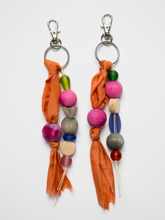 Colorful handmade keychains with wood and glass beads and silk on a white background