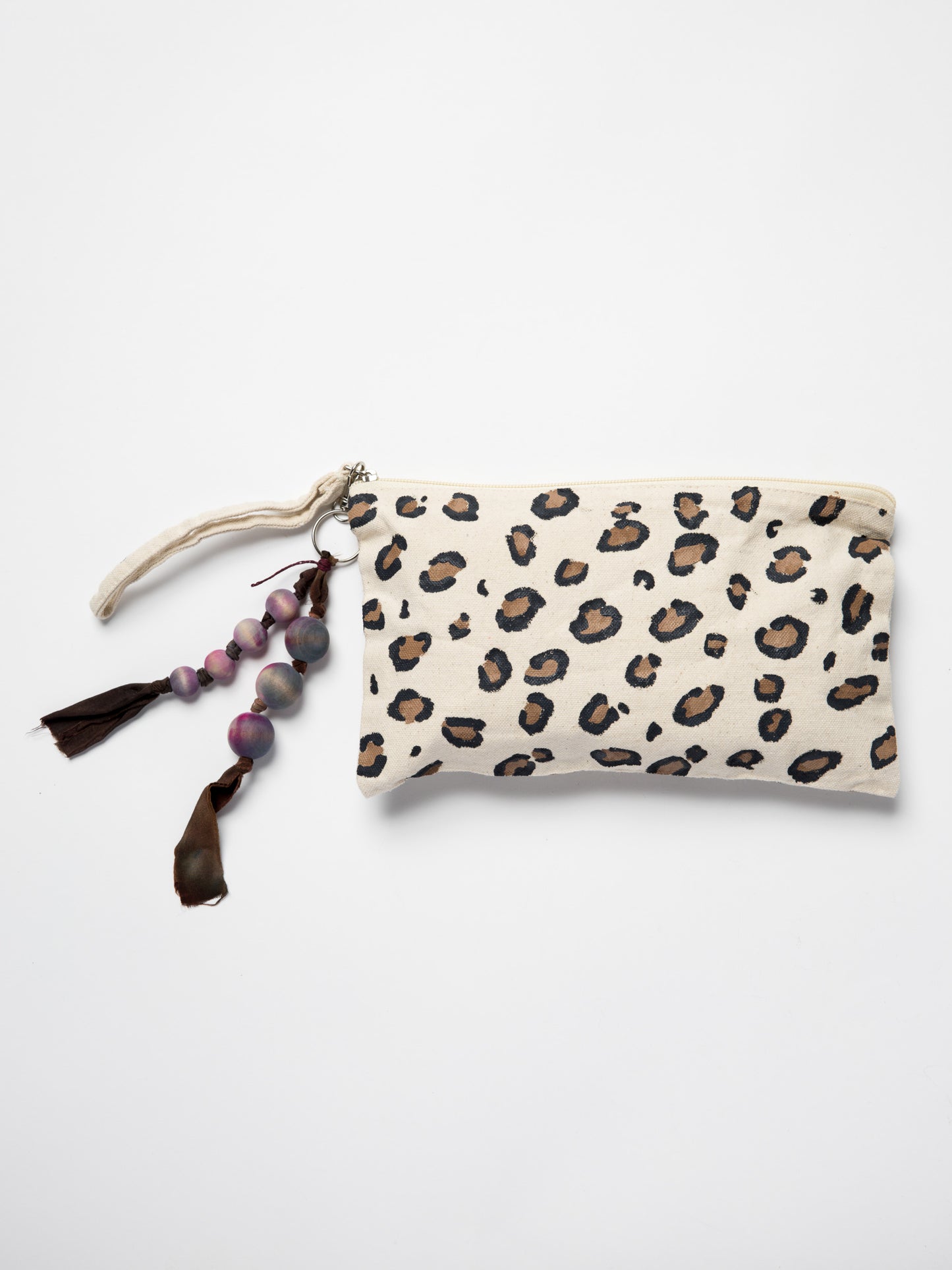 Handmade bag charm made with wooden beads and silk ribbons attached to hand painted leopard pouch on a white background