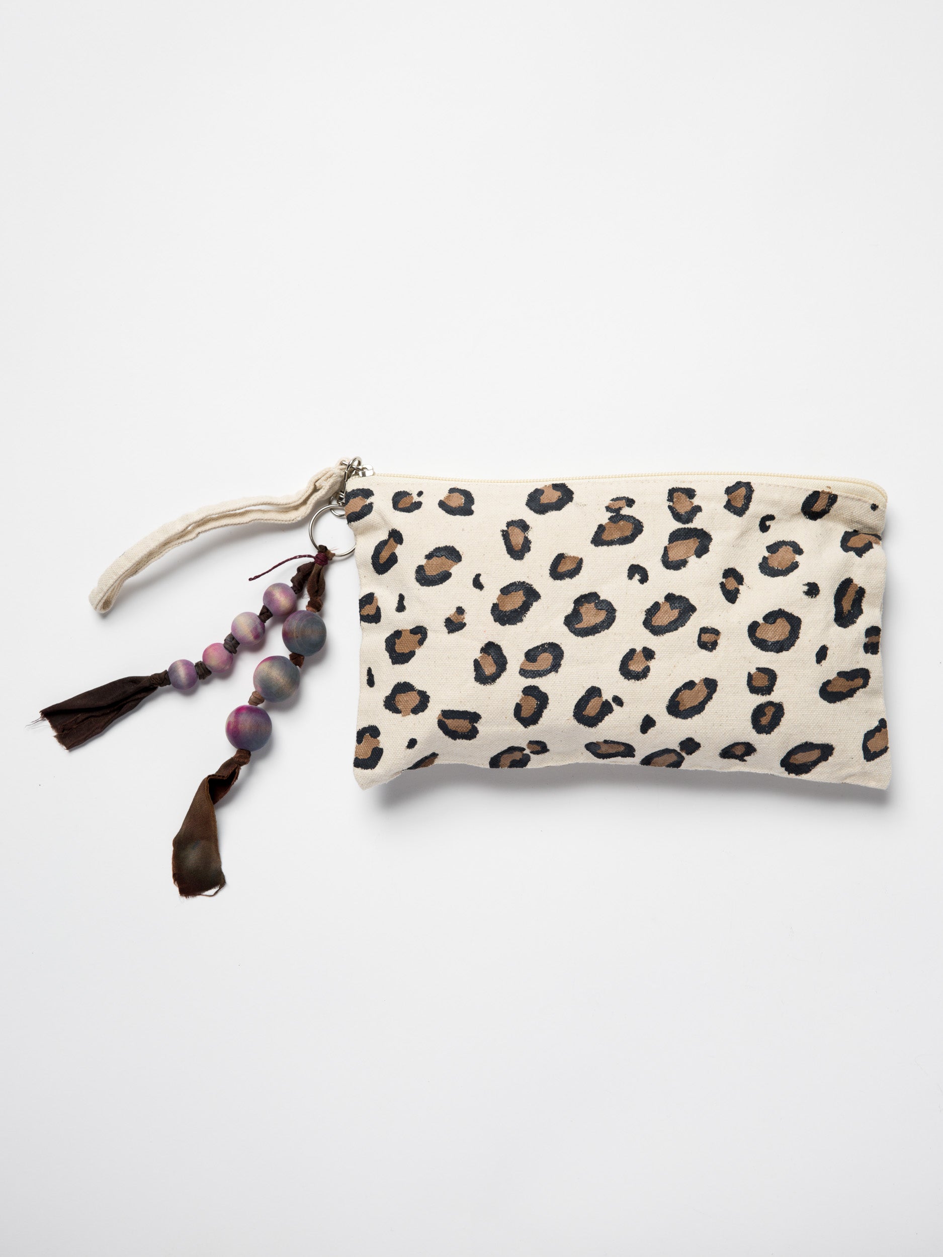Handmade bag charm made with wooden beads and silk ribbons attached to hand painted leopard pouch on a white background