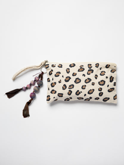 Handmade bag charm made with wooden beads and silk ribbons attached to hand painted leopard pouch on a white background