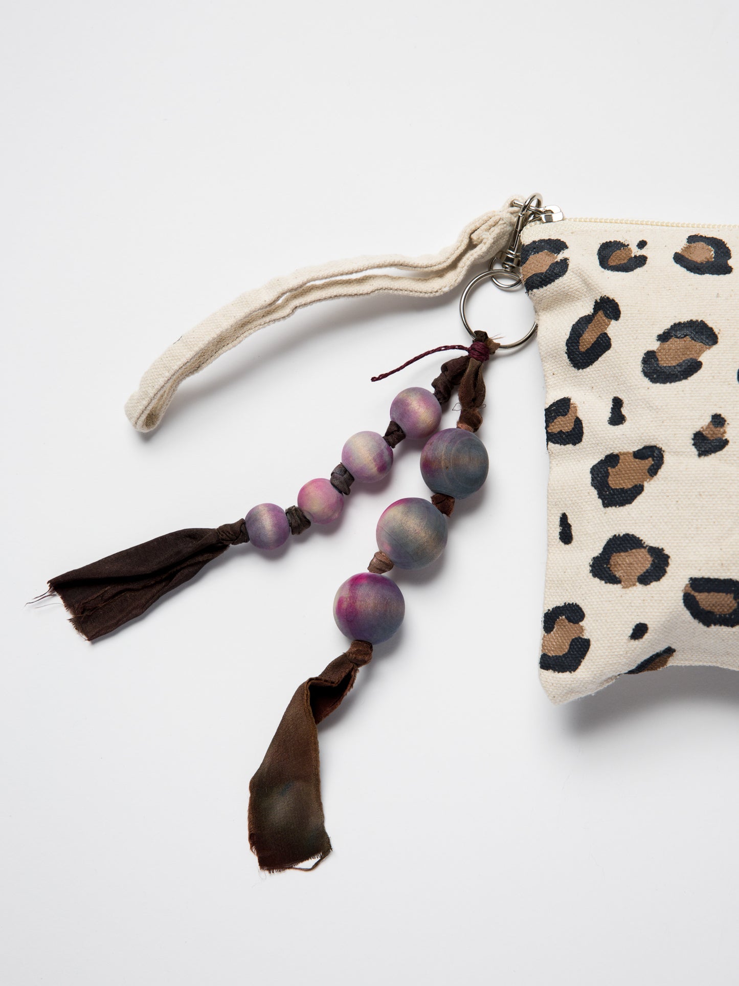 Handmade bag charm made with wooden beads and silk ribbons attached to hand painted leopard pouch on a white background